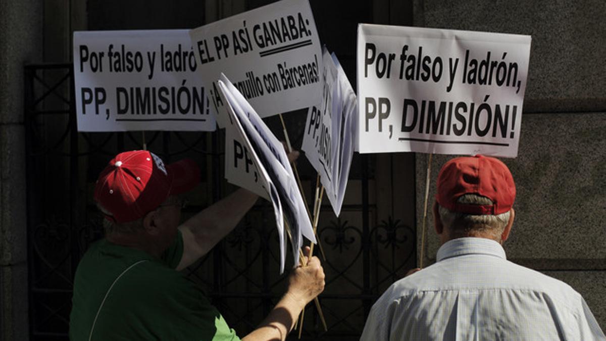 Dos ciudadanos portan pancartas en las que piden dimisiones en el PP.