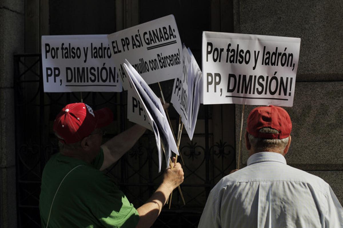 Dos ciutadans porten pancartes en què demanen dimissions al PP.