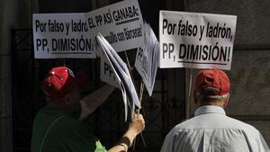 Dos ciudadanos portan pancartas en las que piden dimisiones en el PP.