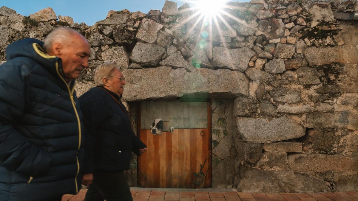 Dos vecinos de Fresnedillas de la Oliva pasan frente a uno de los murales del proyecto 'Casas vivas'.