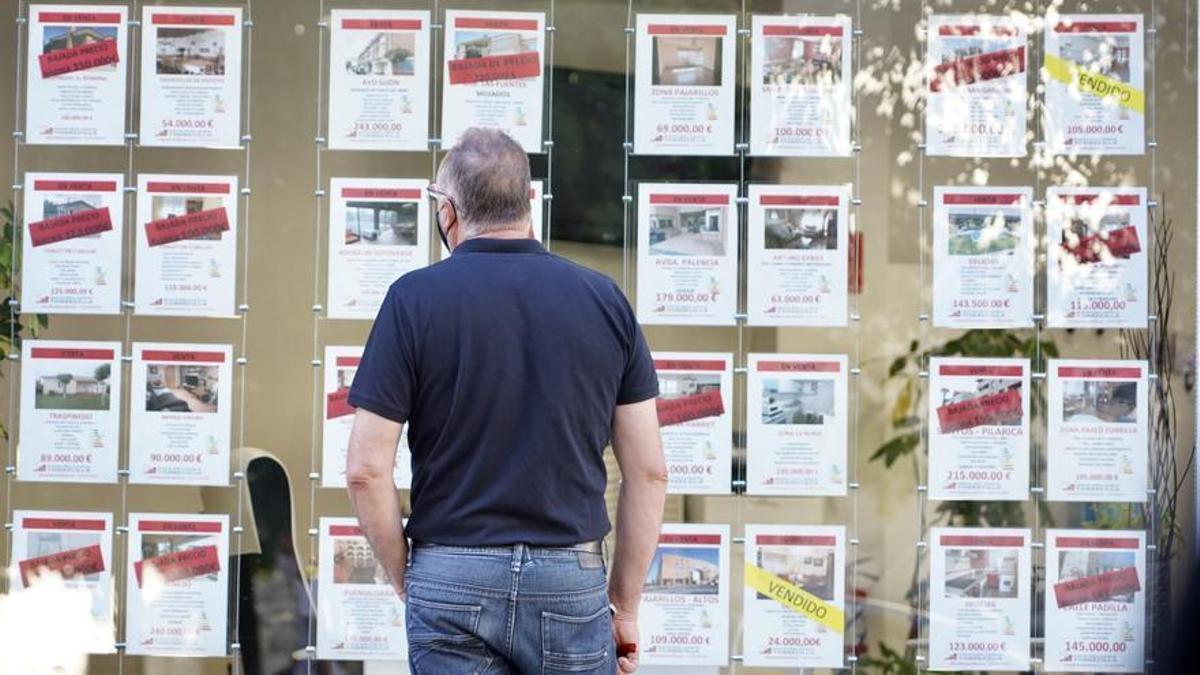 Hombre mirando anuncios de venta o alquiler de viviendas en el escaparate de una inmobiliaria