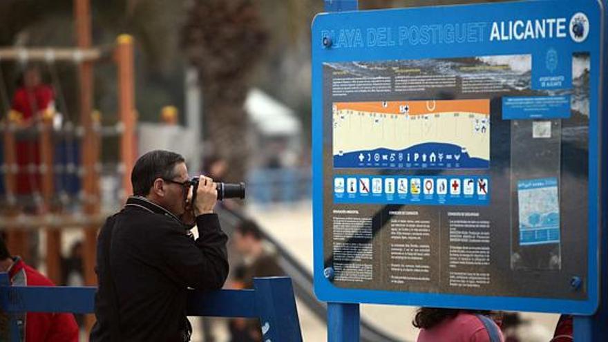 Un turista fotografía el mar desde el paseo de Gómiz, en la playa del Postiguet, junto a un cartel en el que figura un plano de la ciudad.