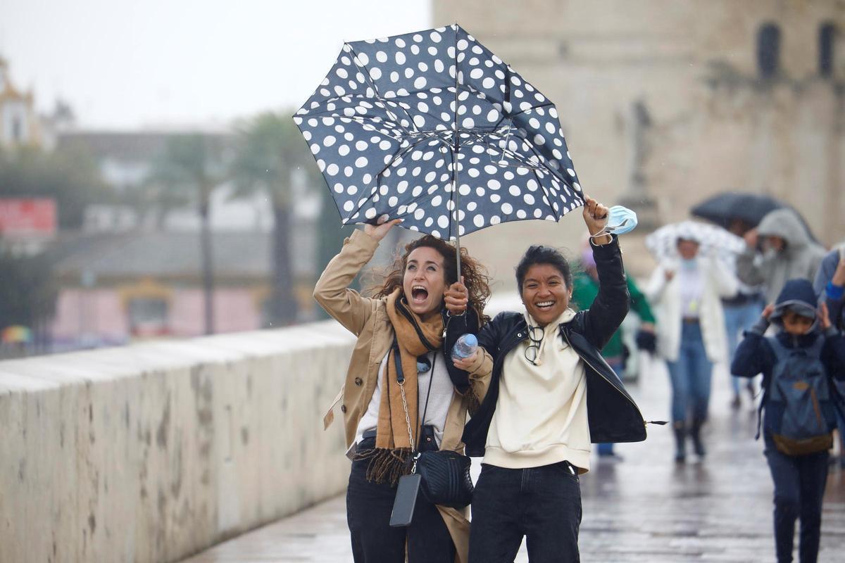Dos turistas intentan protegerse de la lluvia y el viento con su paraguas este sábado en Córdoba.