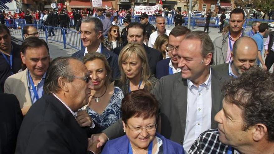 Alberto Fabra saluda al presidente del PP de Castelló, Carlos Fabra, a su llegada al Auditorio de la Diputación de Alicante. Al fondo, la protesta de empleados de RTVV.