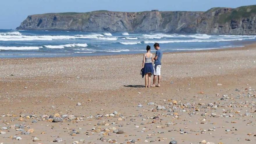 Una pareja pasea por la playa, cubierta de piedras.