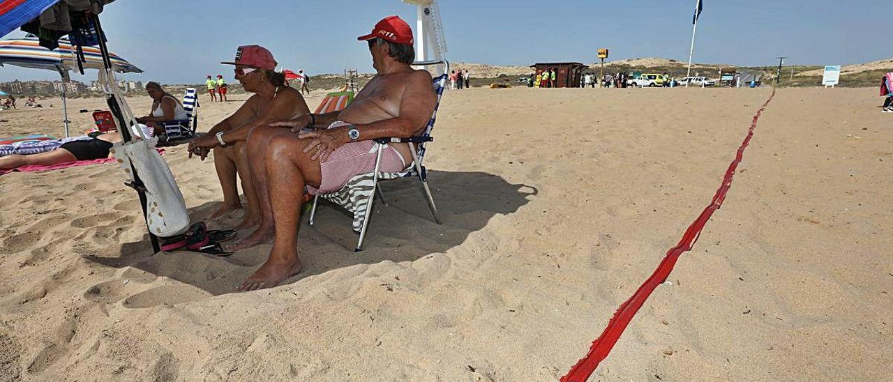 Varios bañistas junto a las cintas rojas que se instalaron ayer en la playa de El Altet. ANTONIO AMORÓS