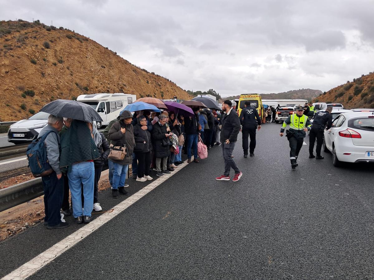 Pasajeros del bus siniestrado que lograron salir por sus propios medios se refugian de la lluvia en el asfalto.