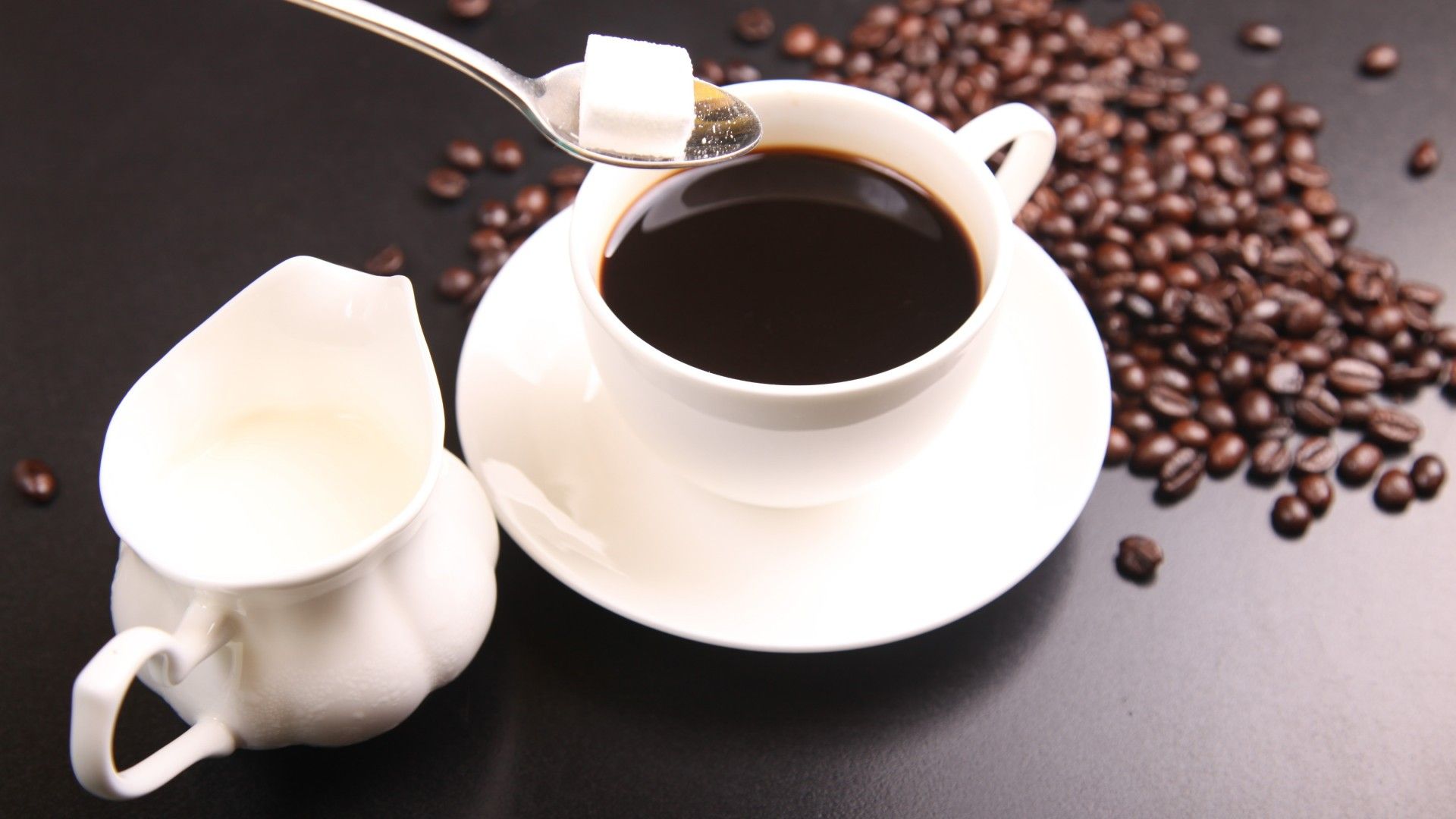 Una taza de café solo con una jarrita de leche y azúcar