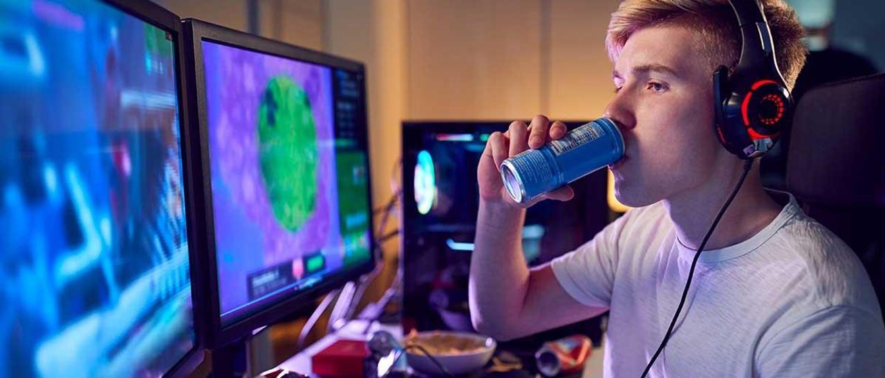 Un joven jugando al ordenador con una bebida energética.