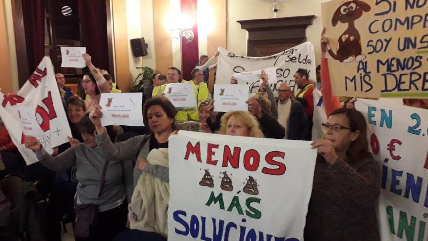 En primer plano, un grupo de personas con pancartas contra el ADN canino, y al fondo policías reclamando mejoras.