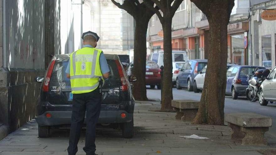 Un policía municipal sanciona a un vehículo mal aparcado en la calle San Agustín.