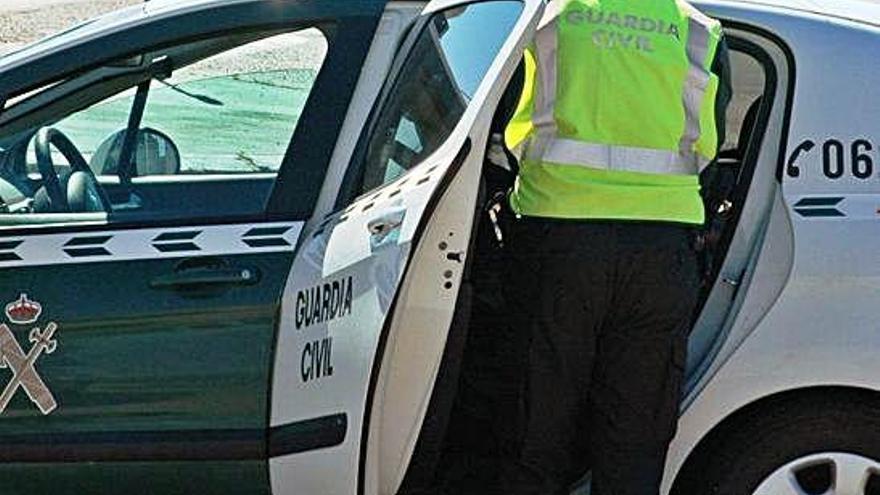 Un agente de la Guardia Civil accede a la parte de atrás de un coche patrulla.