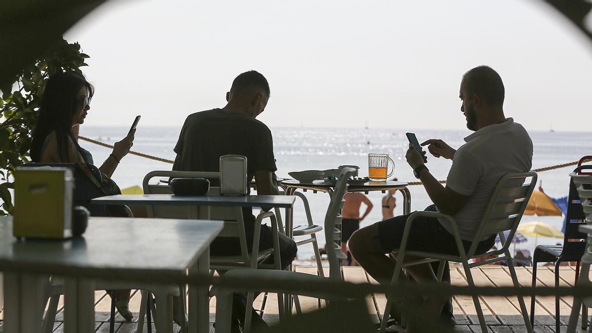 Tres personas consultan sus móviles en una terraza en la playa.