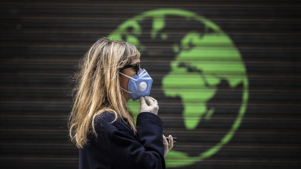 Una mujer protegida con una mascarilla pasa ante una publicidad comercial / coronavirus