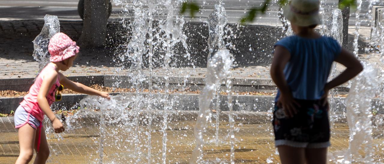 Un niña se refresca, a la sombra, en una fuente de Alicante