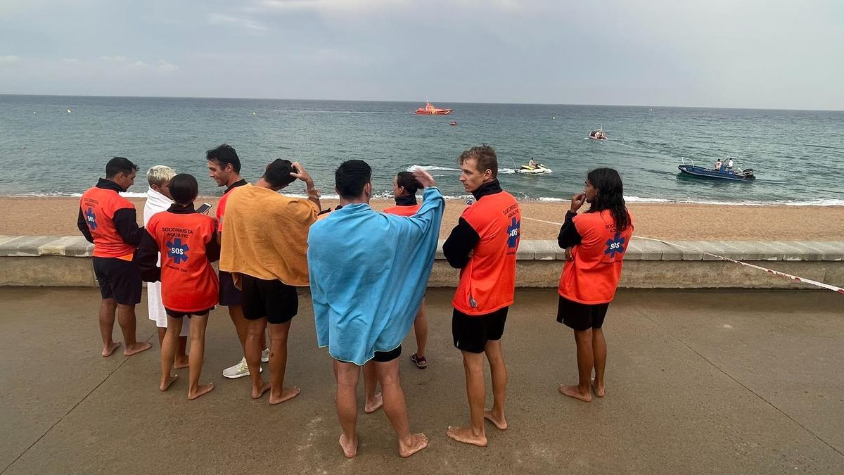 Un grup de socorristes parla amb testimonis mentre al fons, professionals d&#039;emergències biusquen al banyista