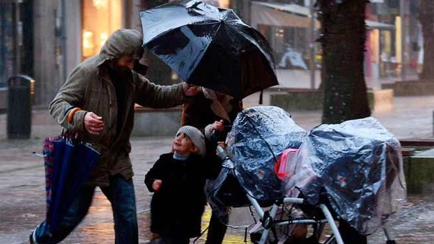 Una familia se protege de la lluvia en una calle de Pontevedra. / RAFA VÁZQUEZ