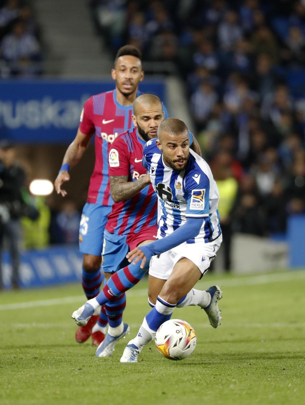 SAN SEBASTIÁN, 21/04/2022.- El centrocampista de la Real Sociedad Rafinha Alcántara (d) escapa de Dani Alves (c), del FC Barcelona, durante el partido de Liga en Primera División que disputan hoy jueves en el Reale Arena, en San Sebastián. EFE/Juan Herrero