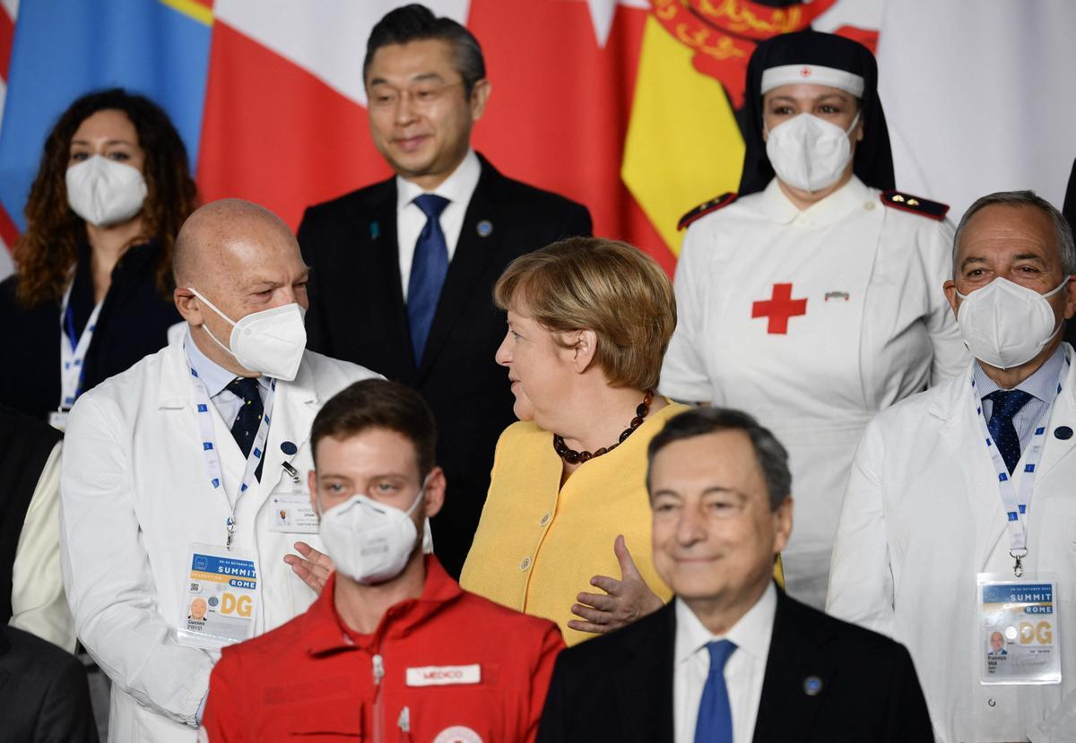 La canciller saliente de Alemania, Angela Merkel, habla con un trabajador de la salud durante una foto grupal de líderes mundiales en la Cumbre del G20.