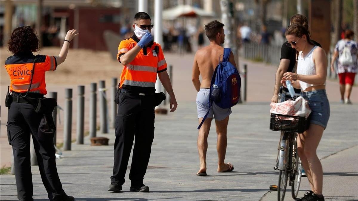 Unos agentes cívicos reclaman a una chica que se coloque la mascarilla, este sábado, en la Barceloneta.