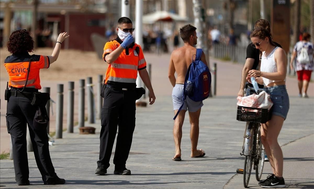 Unos agentes cívicos reclaman a una chica que se coloque la mascarilla, este sábado, en la Barceloneta.