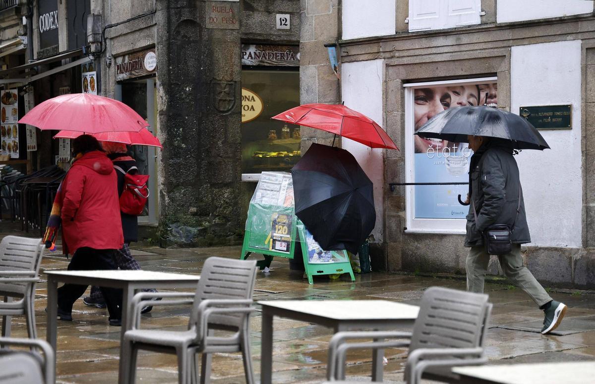 Varias personas transitan frente a una terraza vacía en un día de lluvia en la zona monumental de Santiago