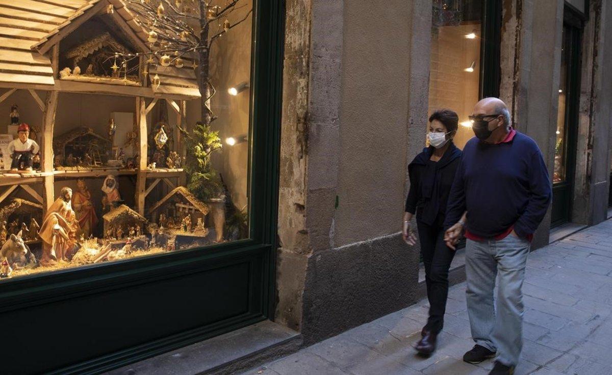 Una pareja con mascarilla pasea por el centro de Barcelona, frente a un establecimiento con motivos navideños.
