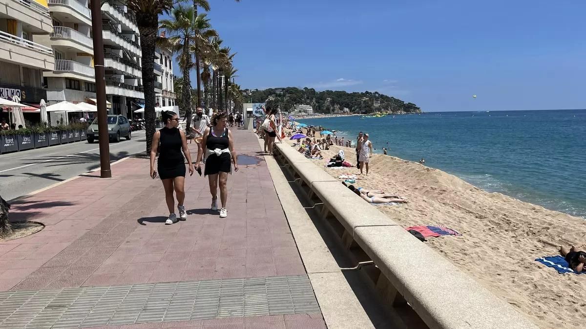 Imatge d'arxiu de dos turistes passejant pel passeig marítim de Lloret de Mar mentre miren els banyistes que hi ha a la platja.