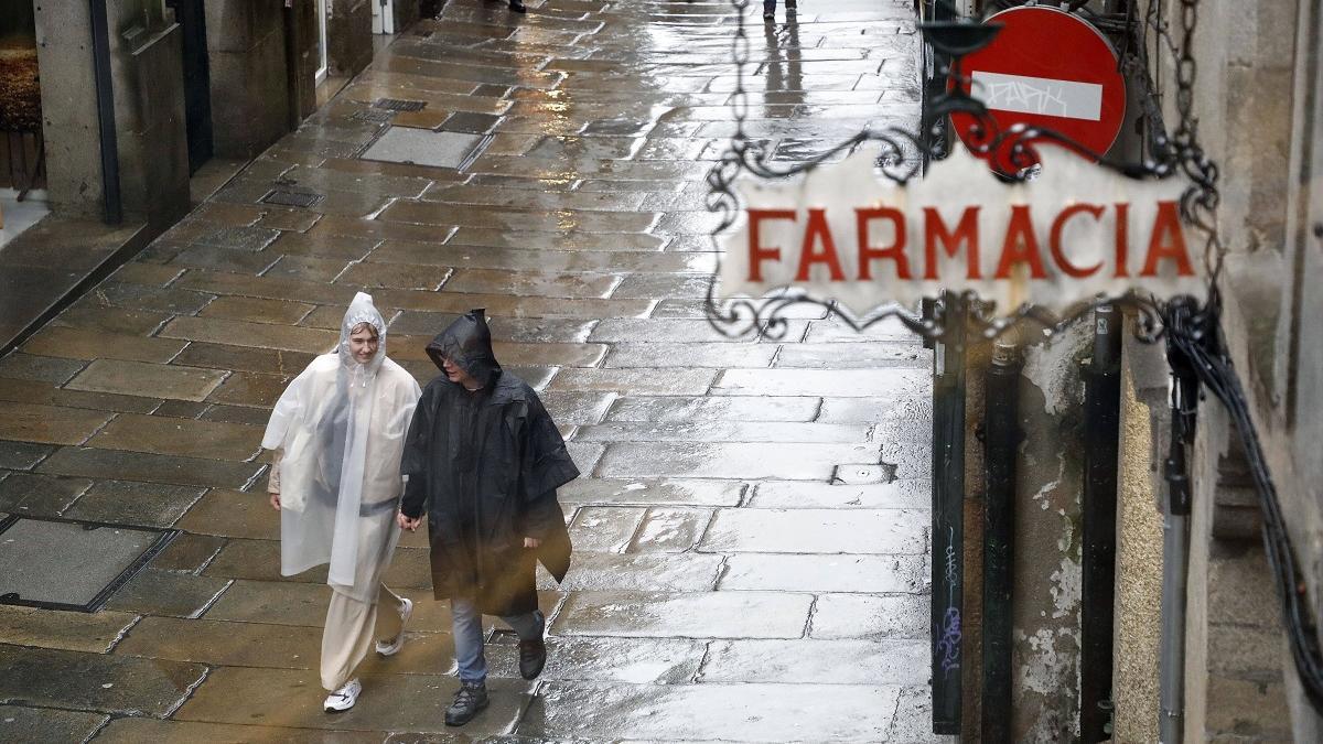 Dos turistas pasean por Compostela ataviados con ponchos para la lluvia