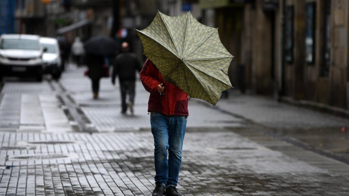 Un viandante intenta resguardarse del viento y la lluvia bajo su paraguas.