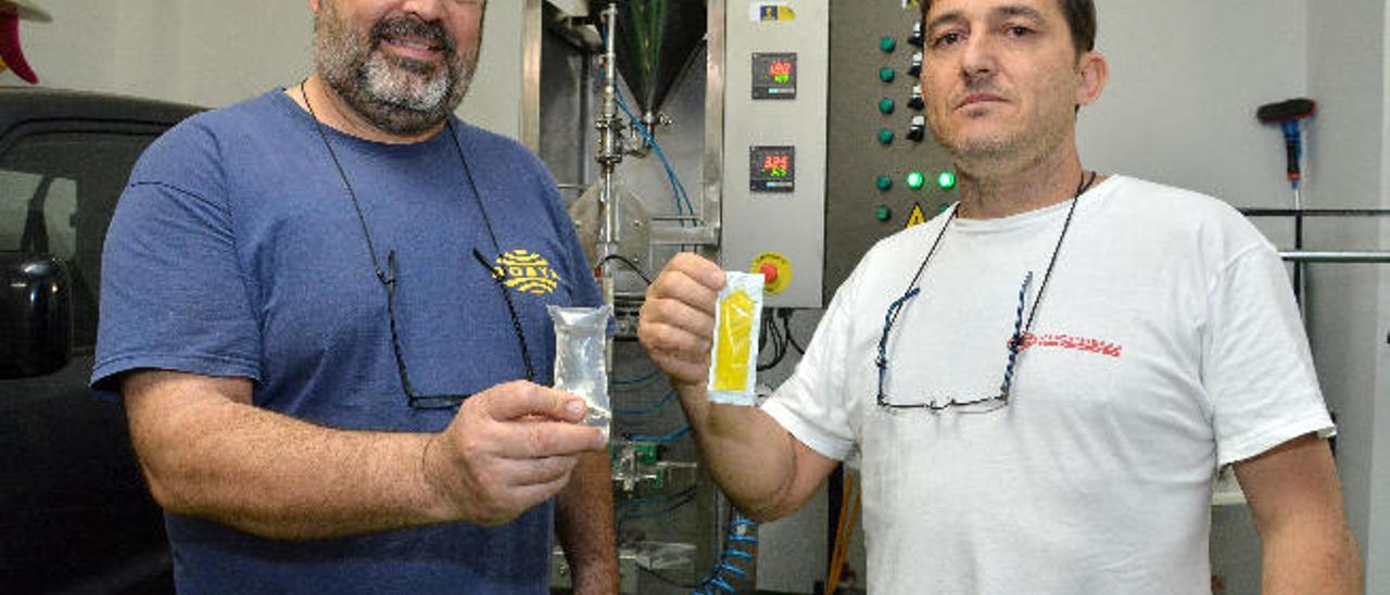 Pedro Suárez y Francisco Cabrera muestran las bolsas de plástico en monodosis obtenidas de las pruebas con la máquina inventada detrás de ellos.