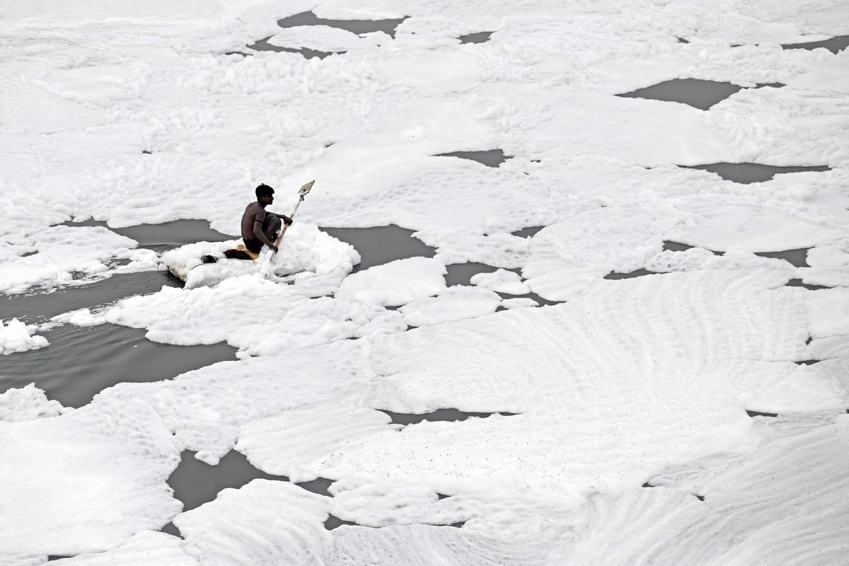 Un hombre rema con su balsa para recoger materiales reciclables en las aguas del río Yamuna, lleno de espuma contaminada, en Nueva Delhi, India. Imagen del 5 de julio del 2022.