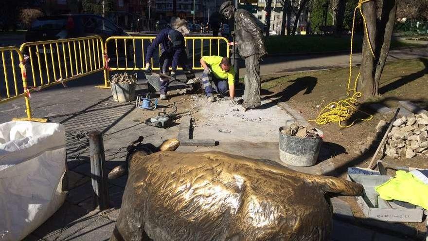 Dos empleados municipales cavan a los pies de la escultura del tratante para arrancarla del suelo; en primer término, el xato, ya retirado del lugar que ocupaba en la parte alta del parque del Carbayedo.