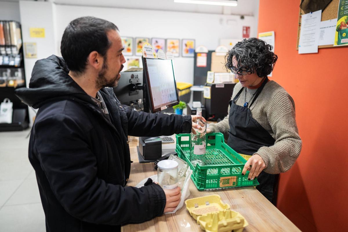Un cliente devuelve un envase de vidrio en el supermercado cooperativa Foodcoop BCN, que ya tiene implementado el sistema de retorno de envases de cristal de agua, yogur y leche.