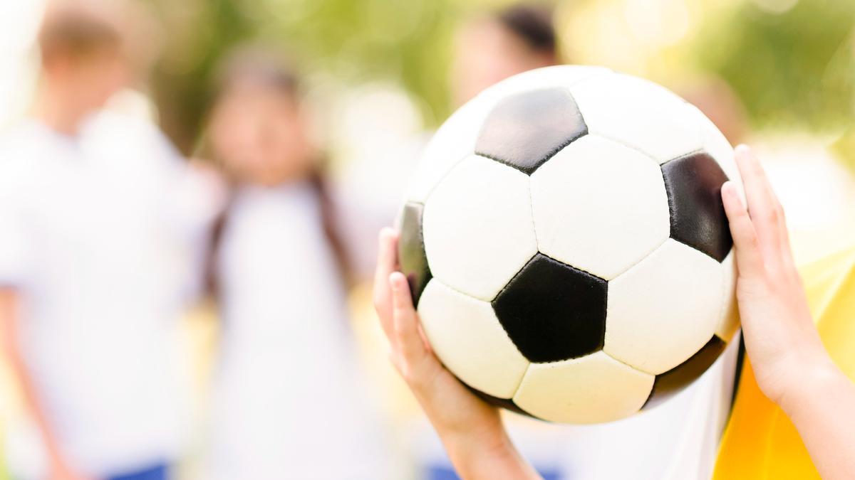 Una niña sostiene un balón de fútbol en un campo de fútbol.