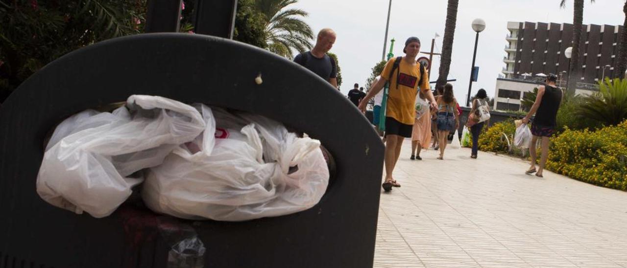 Turistas paseando junto a una papelera llena de basura en el entorno de la playa del Postiguet. RAFA ARJONES