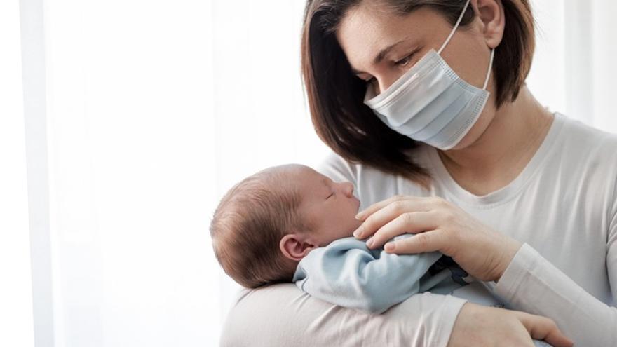 Una madre, con mascarilla, sostiene a su bebé.