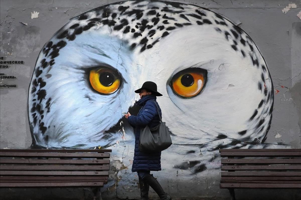 Una mujer camina frente a un grafiti de un buho, en el centro de Moscú, Rusia.