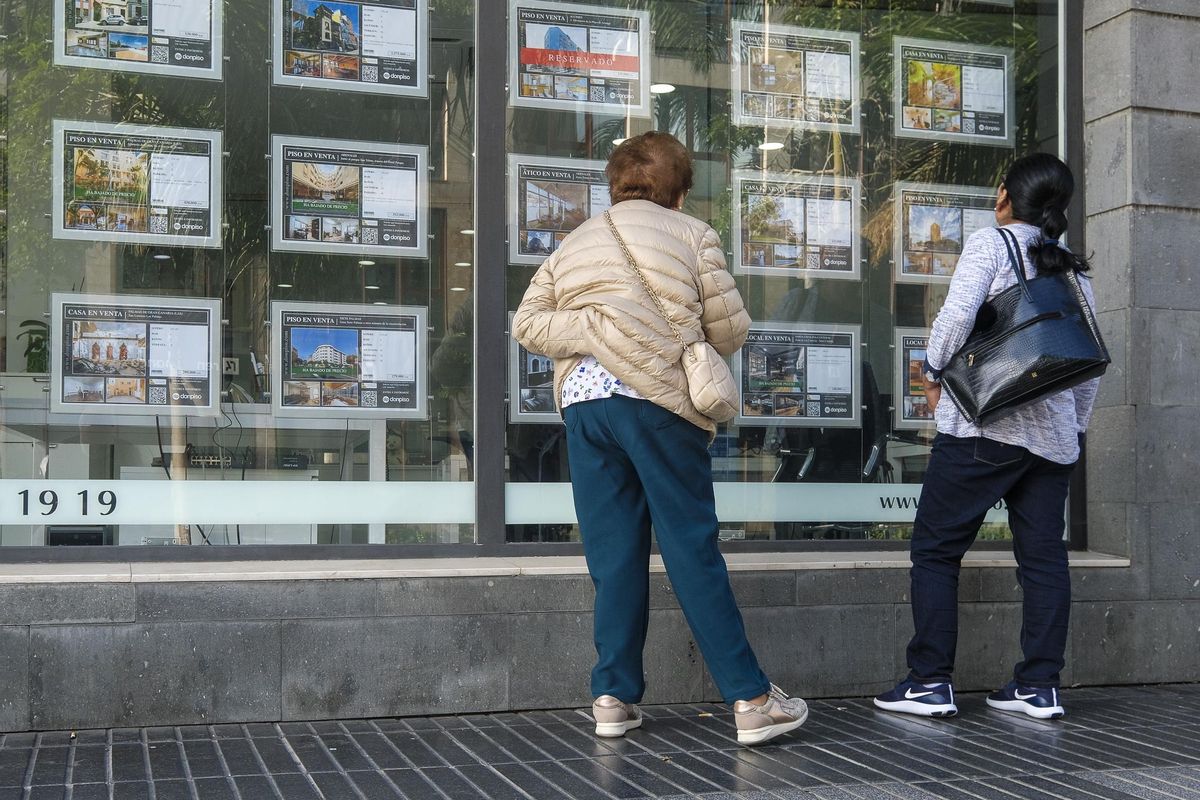 Varias personas miran casas en venta en el escaparate de una inmobiliaria.