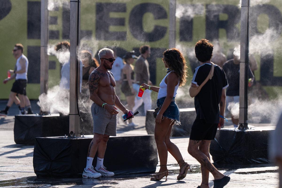 Barcelona. Asistentes al primer día del Brunch Elektronik Festival se refrescan bajo los nebulizadores de agua instalados en el recinto para combatir las altas temperaturas durante la celebración del evento. 7 de agosto de 2026. Cultura. AUTOR: ZOWY VOETEN