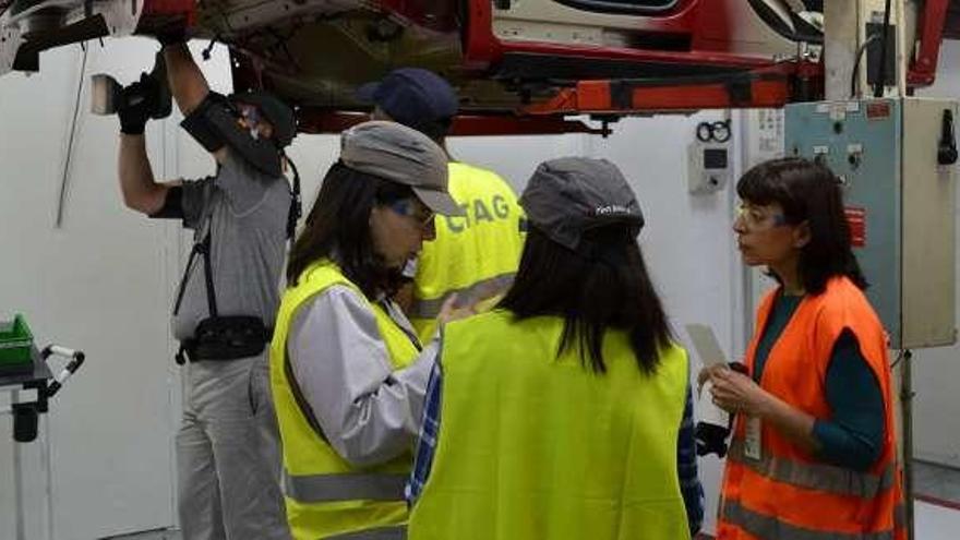 Un operario (i.) prueba un exoesqueleto en presencia de técnicos de PSA, el CTAG y Mutua Universal en un puesto bajo caja en Montaje.