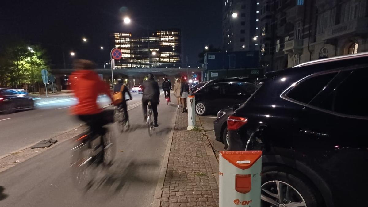 Ciudadanos, ayer noche, desplazándose en bicicleta por las calles de Copenhague, pasando junto a uno de los numerosos puntos de recarga para los vehículos eléctricos.