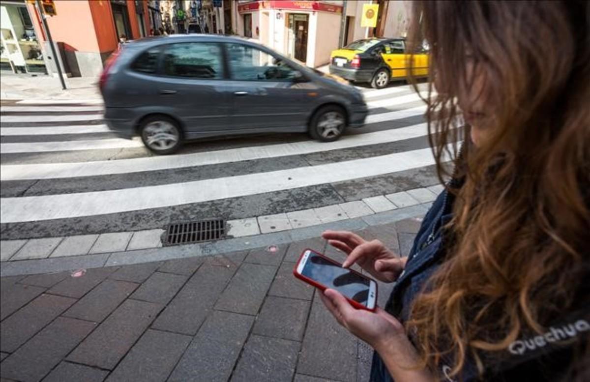 Una joven mira el móvil junto al paso de peatones de Sant Cugat con semáforo en el suelo.