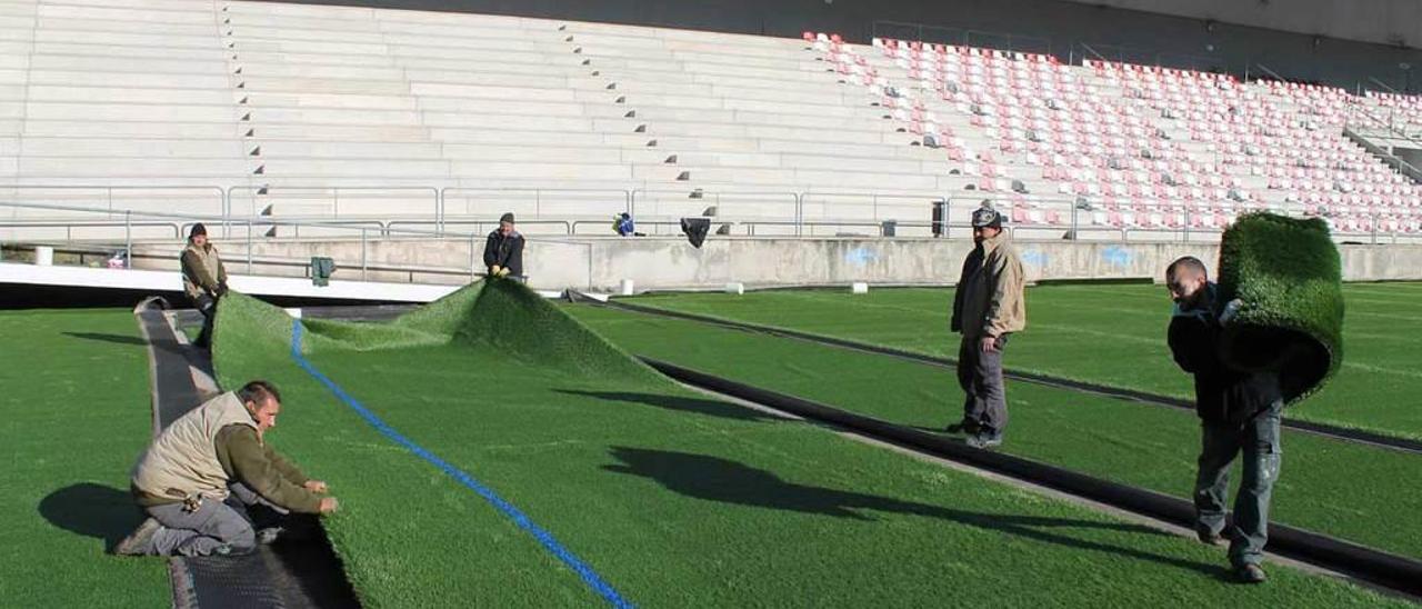 Los operarios terminan de colocar el nuevo césped artificial en el campo municipal de El Bayu.