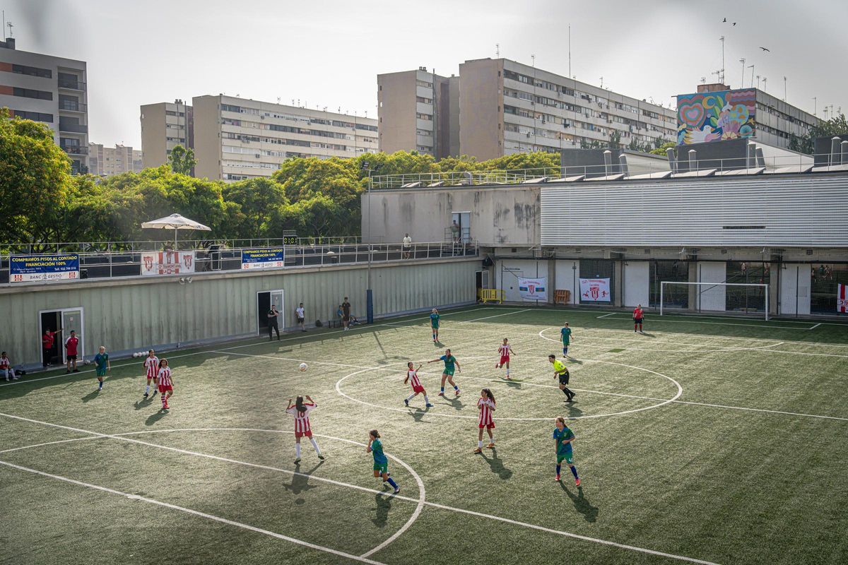 El equipo infantil femenino del Tramontana La Mina jugando contra el Pomar, con los bloques del barrio al fondo.