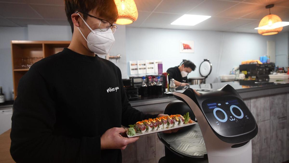 El robot, cuyo nombre comercial es BellaBot, junto a dos trabajadores del restaurante japonés. | ISRAEL SÁNCHEZ