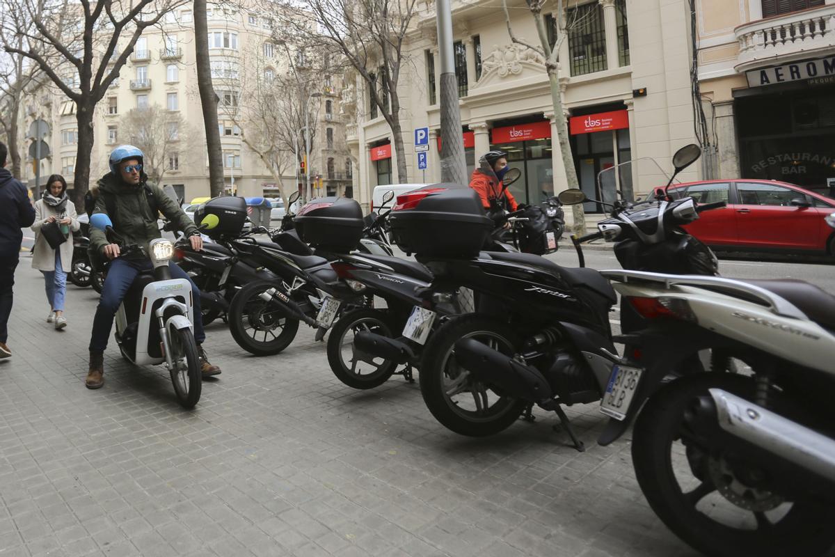 Motos mal aparcadas en una manzana del Eixample. Deberían estar en paralelo a la calzada y no en batería. Y el motorista de la foto debería ir arrastrando la moto por la acera