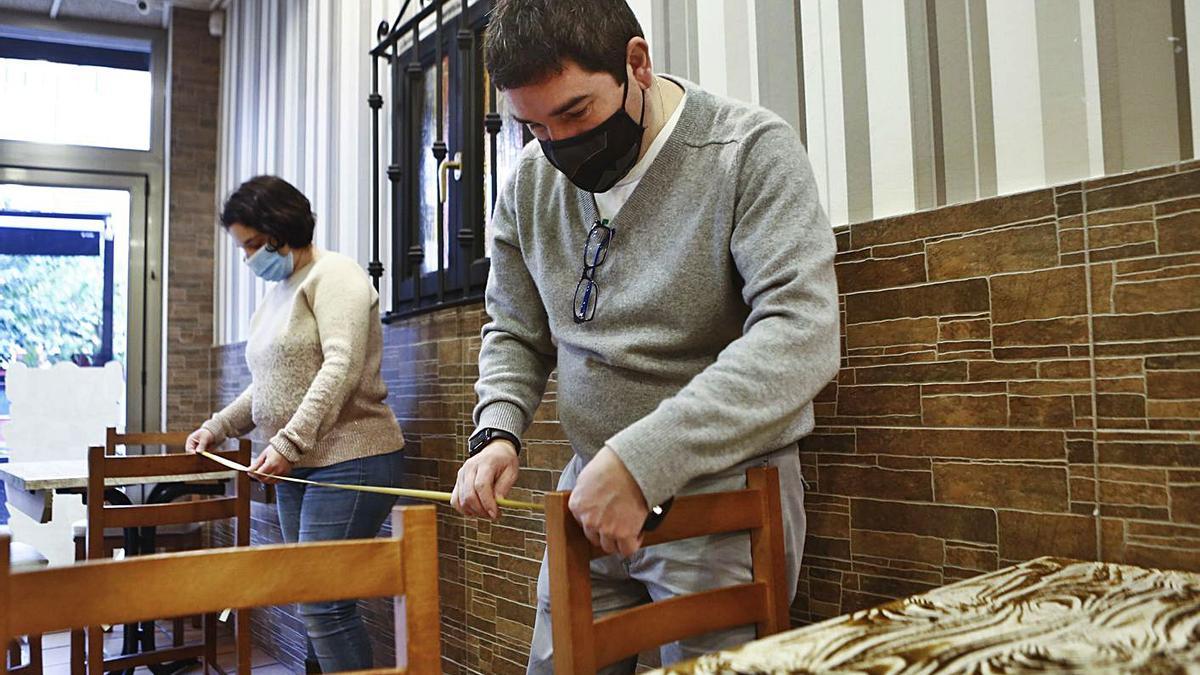 Los hosteleros Annalisa Lusso y Joaquín Fernández, midiendo la distancia entre dos sillas en su bar del barrio ovetense de Teatinos. | Julián Rus