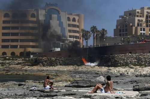 Sunbathing tourists watch firefighters tackle a blaze which broke out in a semi-basement store of the Radisson Blu hotel in St Julian's, outside Valletta