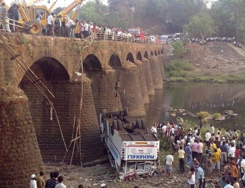 Rescuers and bystanders look at the wreckage of a passenger bus after it fell from a bridge in Ratnagiri district